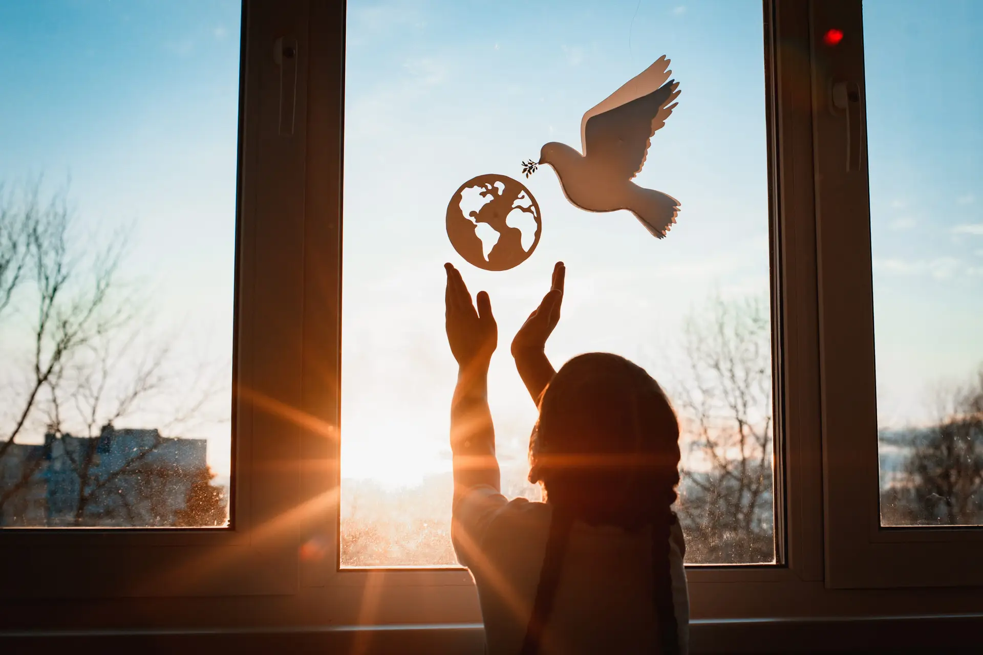 Child reaching toward peace dove and globe silhouette at sunset — international day of living together in peace
